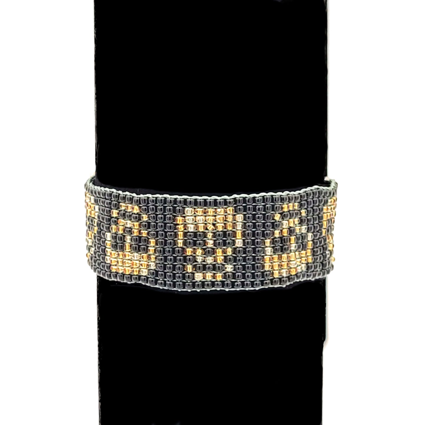 Bracelet made of black, gold colored, and silver colored seed beads with skulls in alternating orientation, on a black velvet bracelet display.