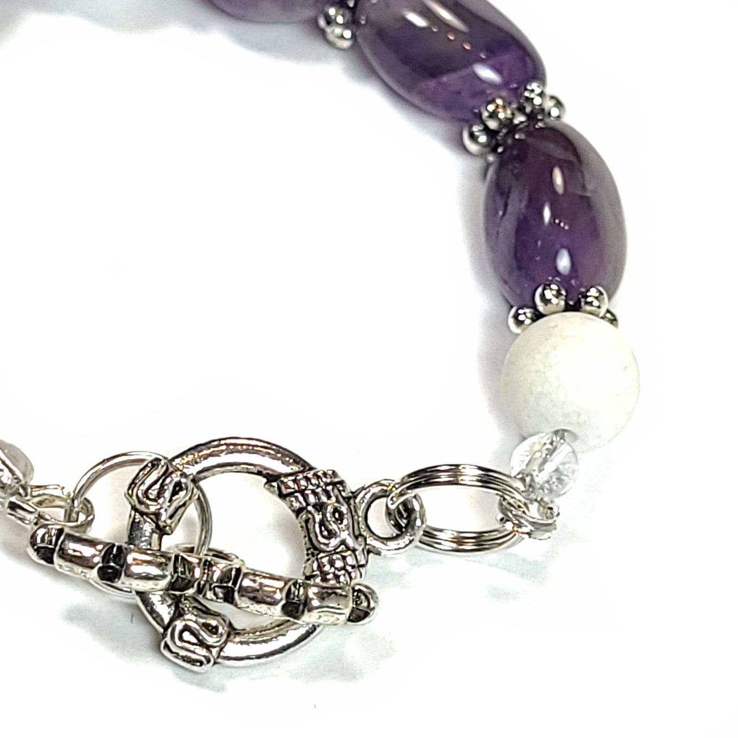 Close up of a silve tone toggle clasp on a bracelet with amethyst pebble beads, white quartz bead, and silver tone spacers.