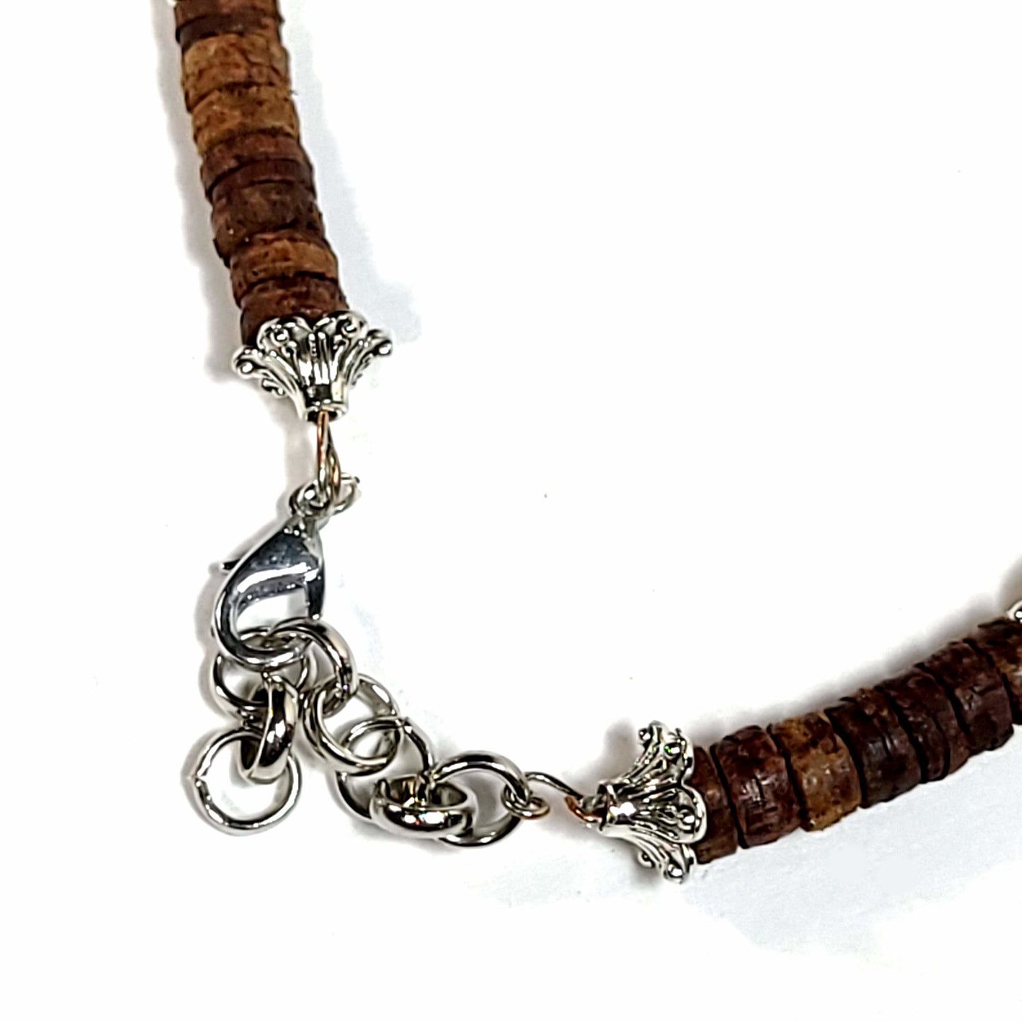 Close up of the clasp on a handmade necklace with heshi shaped coconut shell beads, howlite beads, and matte green fluorite beads highlighted with silver tone spacer beads. End caps are silver tone with lobster clasp and an extender chain.