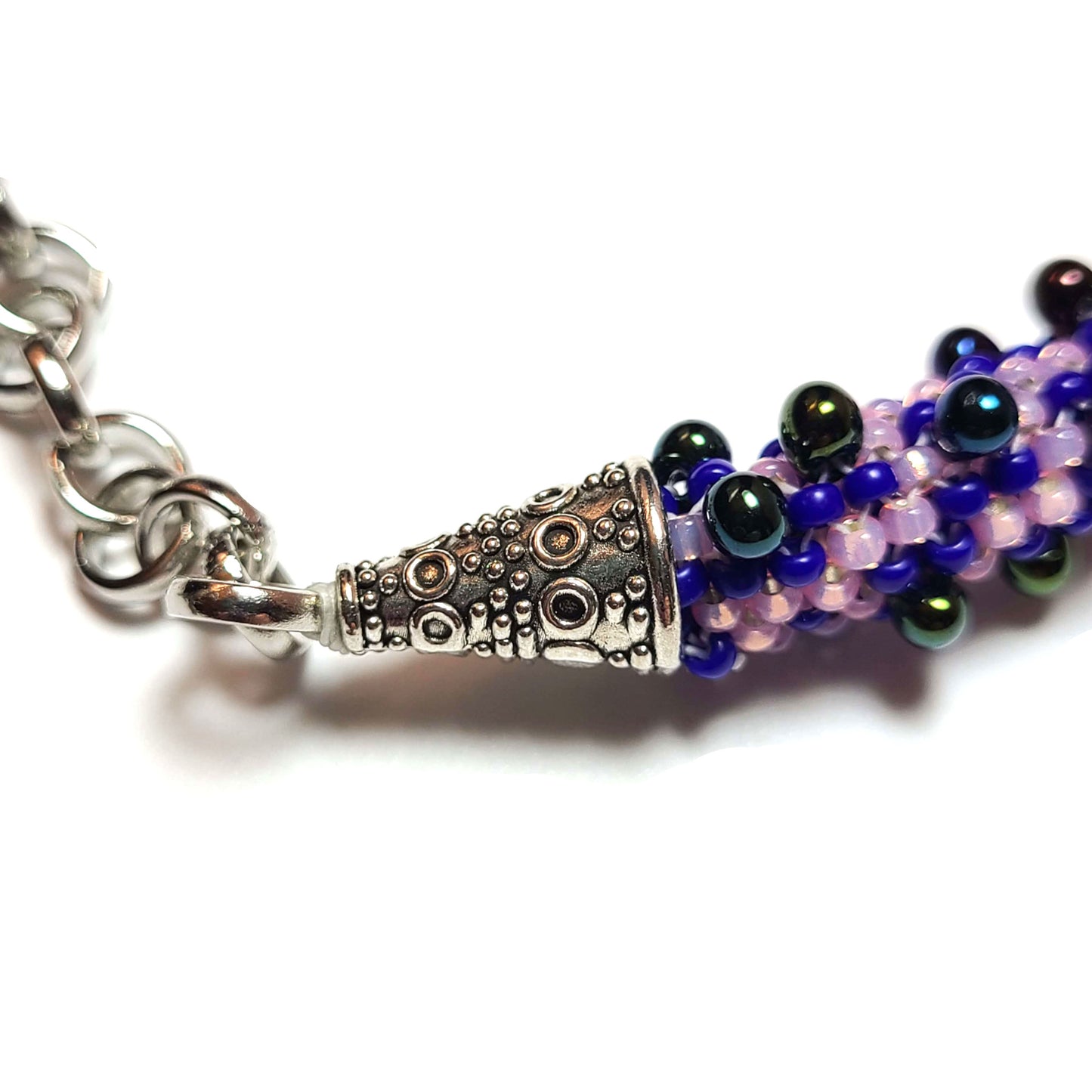 close up of bracelet made of lilac, purple, royal blue, and iridescent black beads with silver color end caps and chain.