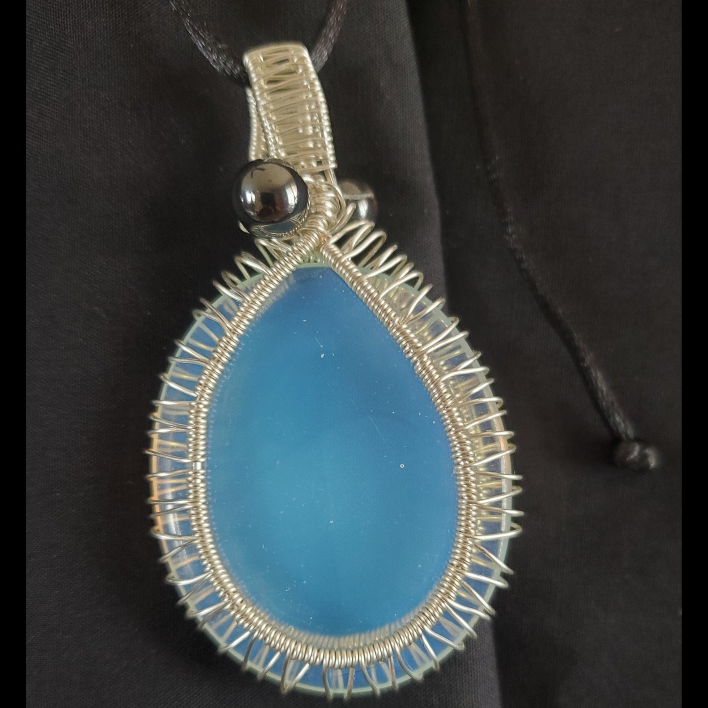 Silver toned wire wrapped Opalite. Comes with a black satin cord with an adjustable slip knot. This stone does have some specks and a scratch, but has very interesting color that really pops, especially on top of dark colors.