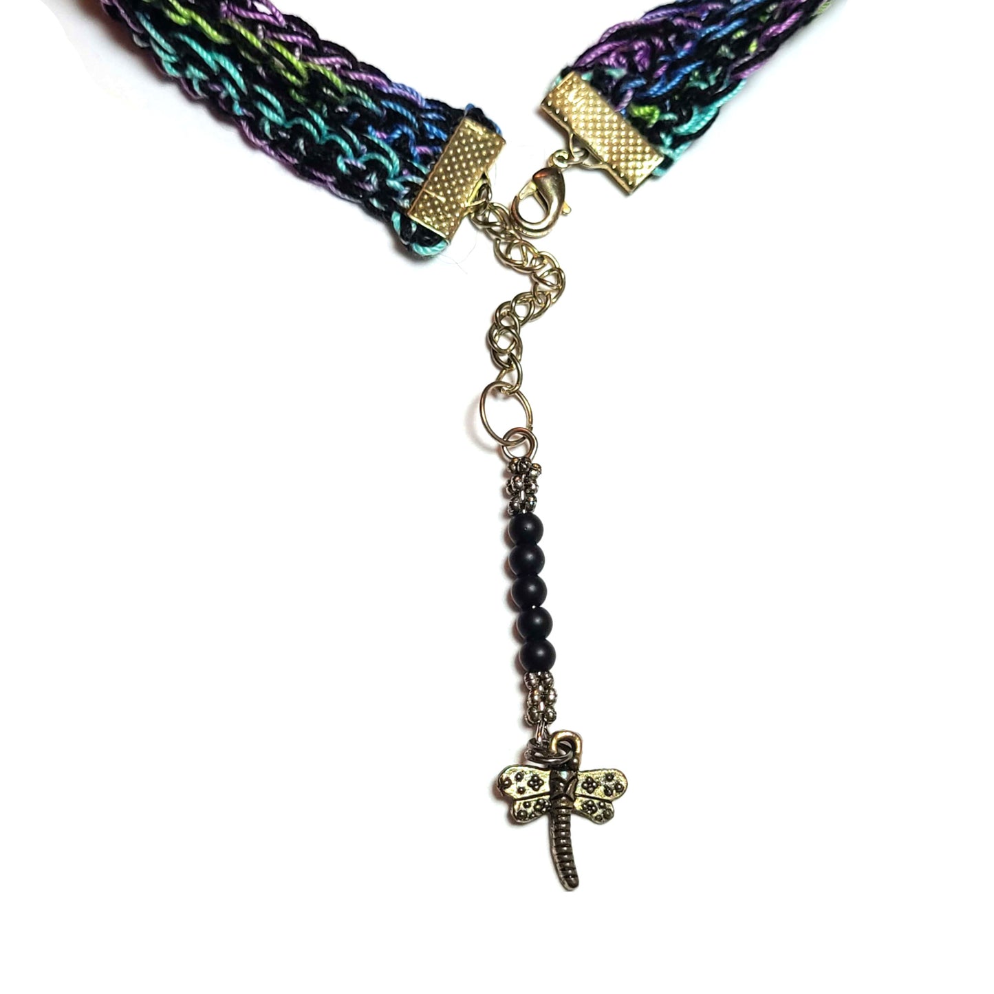 Back view of a crocheted choker that is blue, green, purple, and black with a dragonfly charm on the extension chain with black beads that will dangle down the back of the neck.