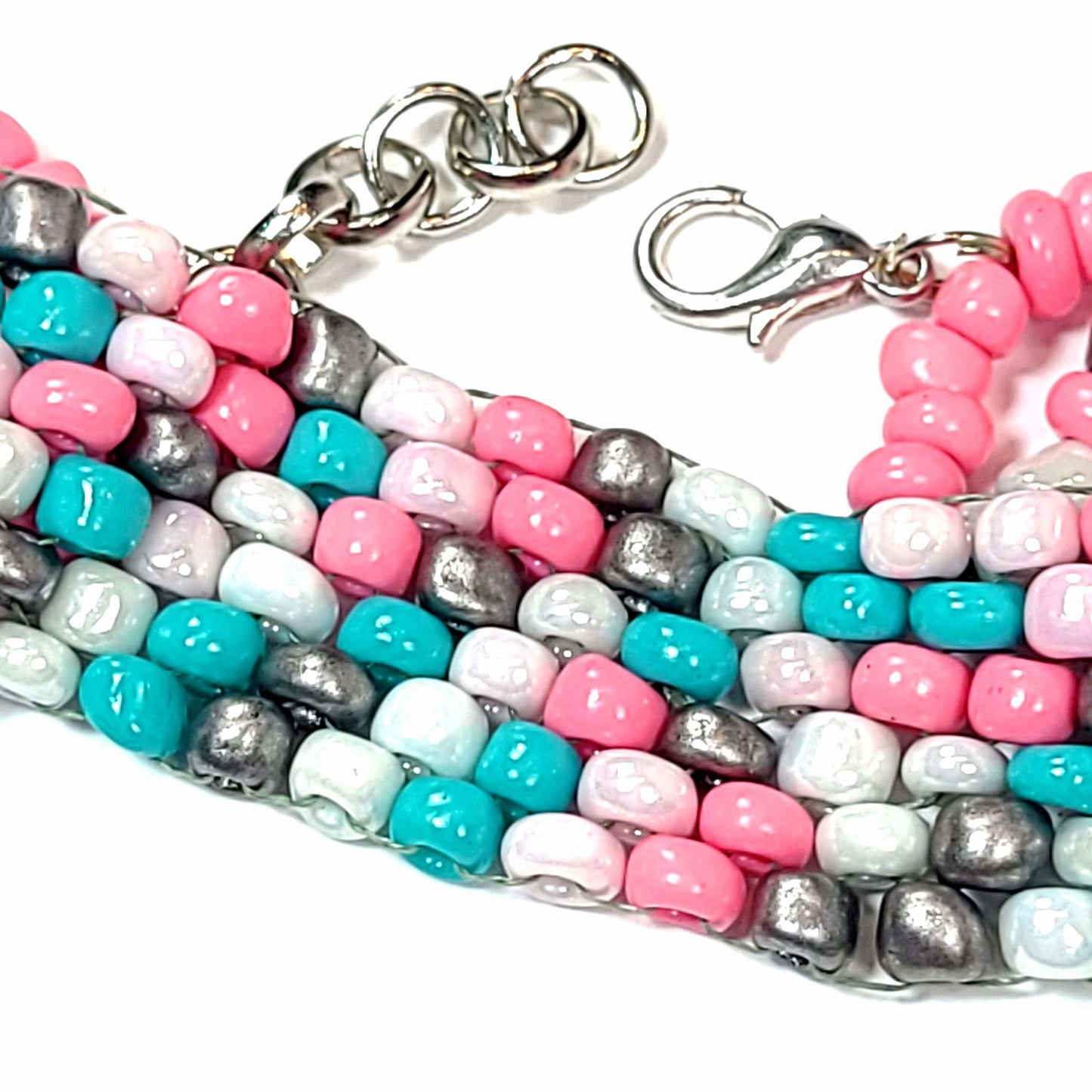 Close up of a bracelet made of pink, white, light blue, and silver colored beads with a silver colored lobster clasp and extension chain.