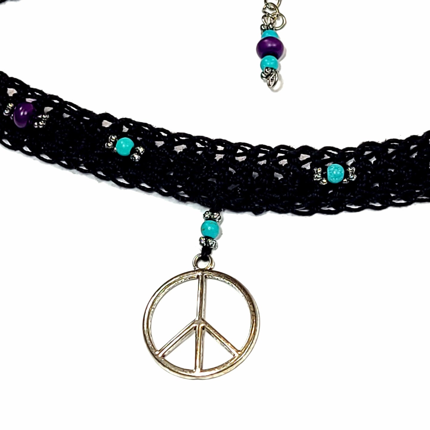 Close up of the front of black crocheted choker with a silver color peace sign charm, silver color spacers, blue beads, and purple beads.
