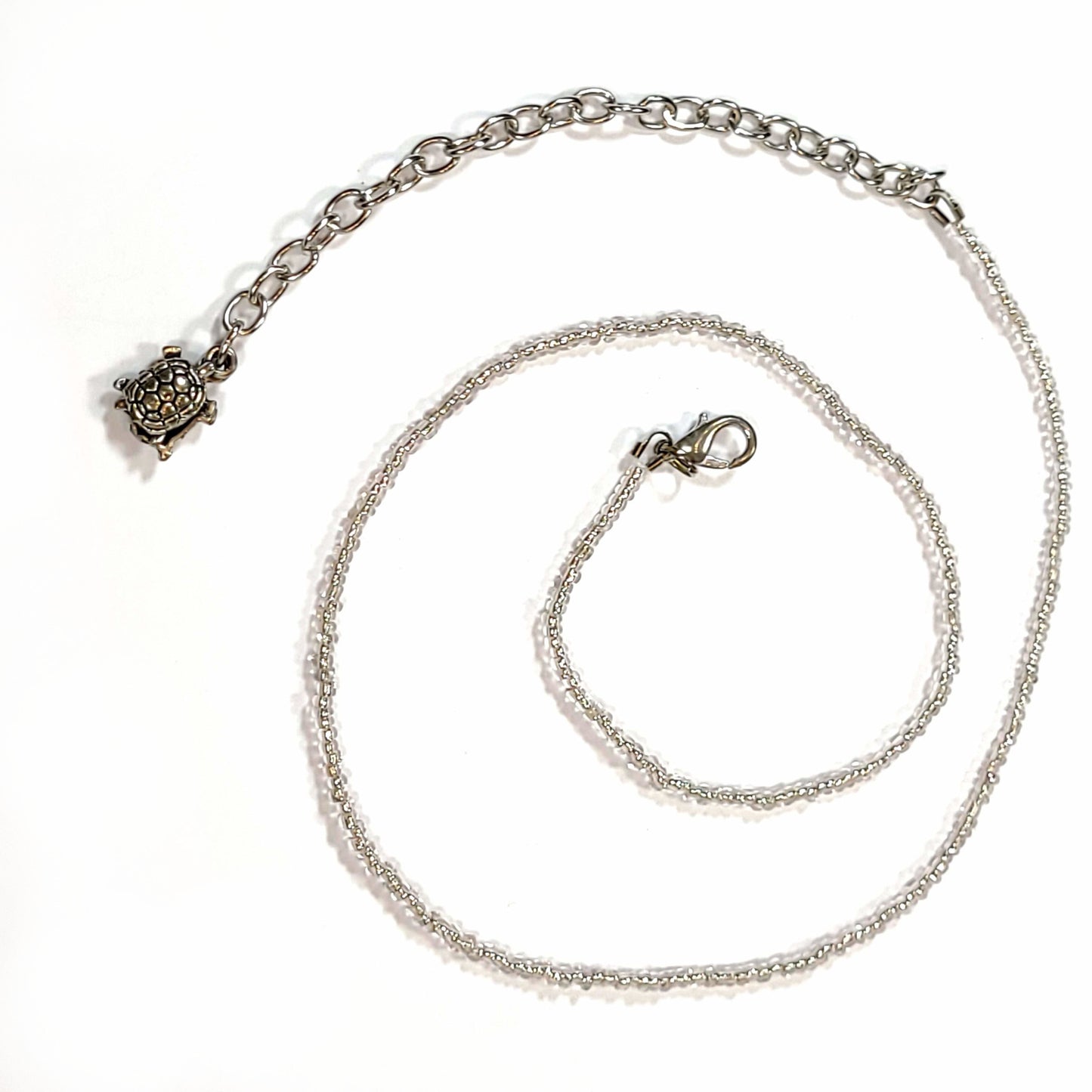 Single strand silver colored seed bead necklace with an extender that has 2 turtle charms on the end.