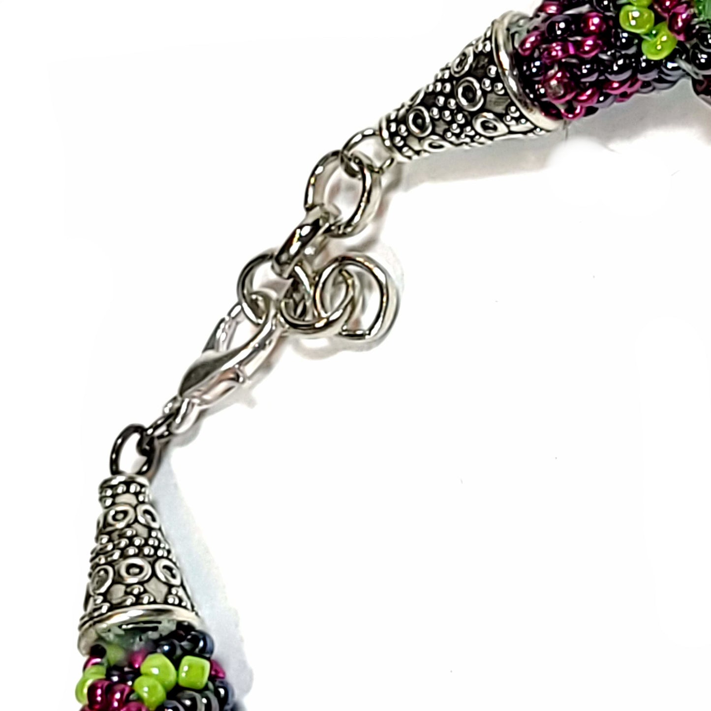 Close up view of the silver color ends and lobster clasp of a Bracelet made of green, orange, and purple bicone beads and light green, magenta, and black seed beads in a spiral pattern with silver color ends and lobster clasp.