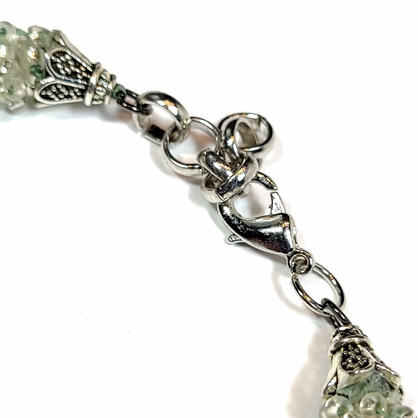 Close up view of the clasp of a Bracelet made of teal, navy, light green, light blue, sand and crystal bicone beads with silver tone seed beads. It also has silver tone end caps, lobster clasp and extender chain.
