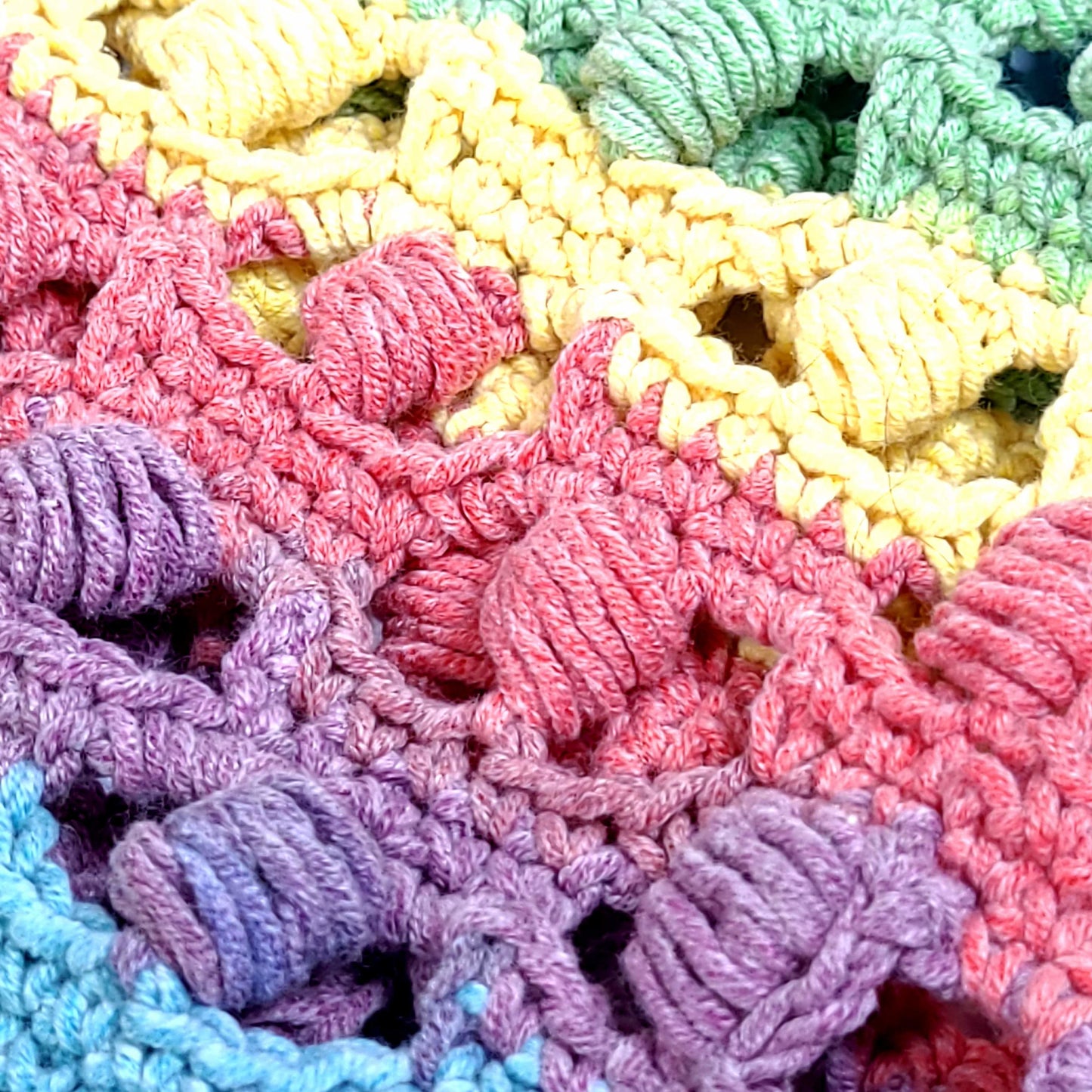 Close up view of a Multi-color hand crocheted tote bag. Made from Caron Cakes yarn and a pattern by Tonya from Nana's Crafty Home. The yarn colors are: lilac, yellow, light blue, peach, and light green.