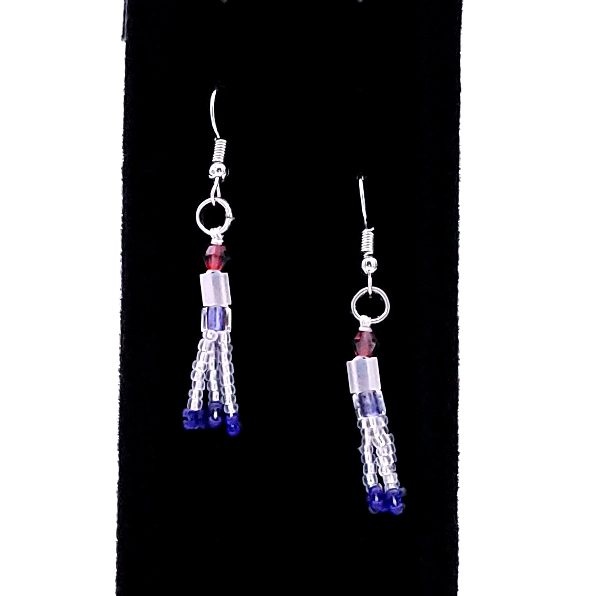 Dangly earrings made of read, white, and blue beads on a black display.