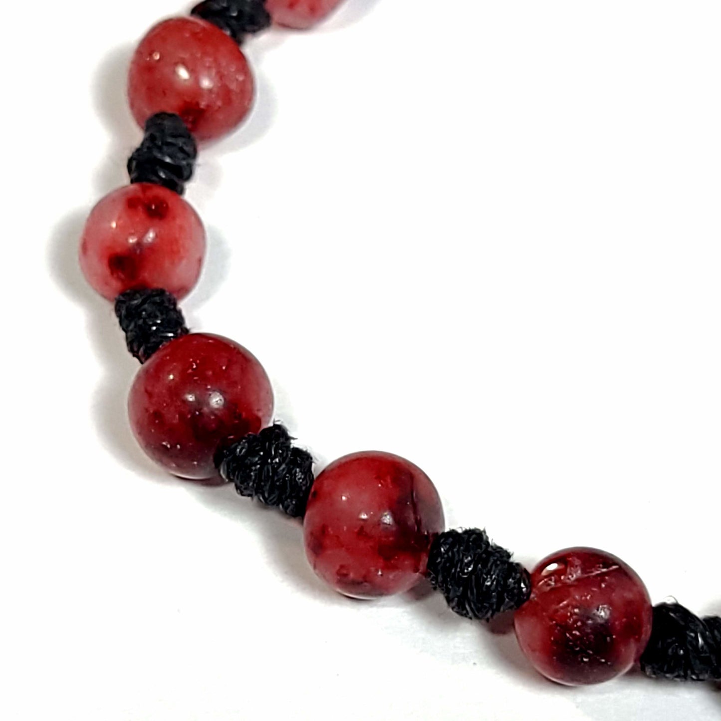 Close up of a Handmade knotted bracelet of red stone beads with white and a little black running through them, Can be worn as a bracelet or anklet. Adjustable slip knot makes adjusting