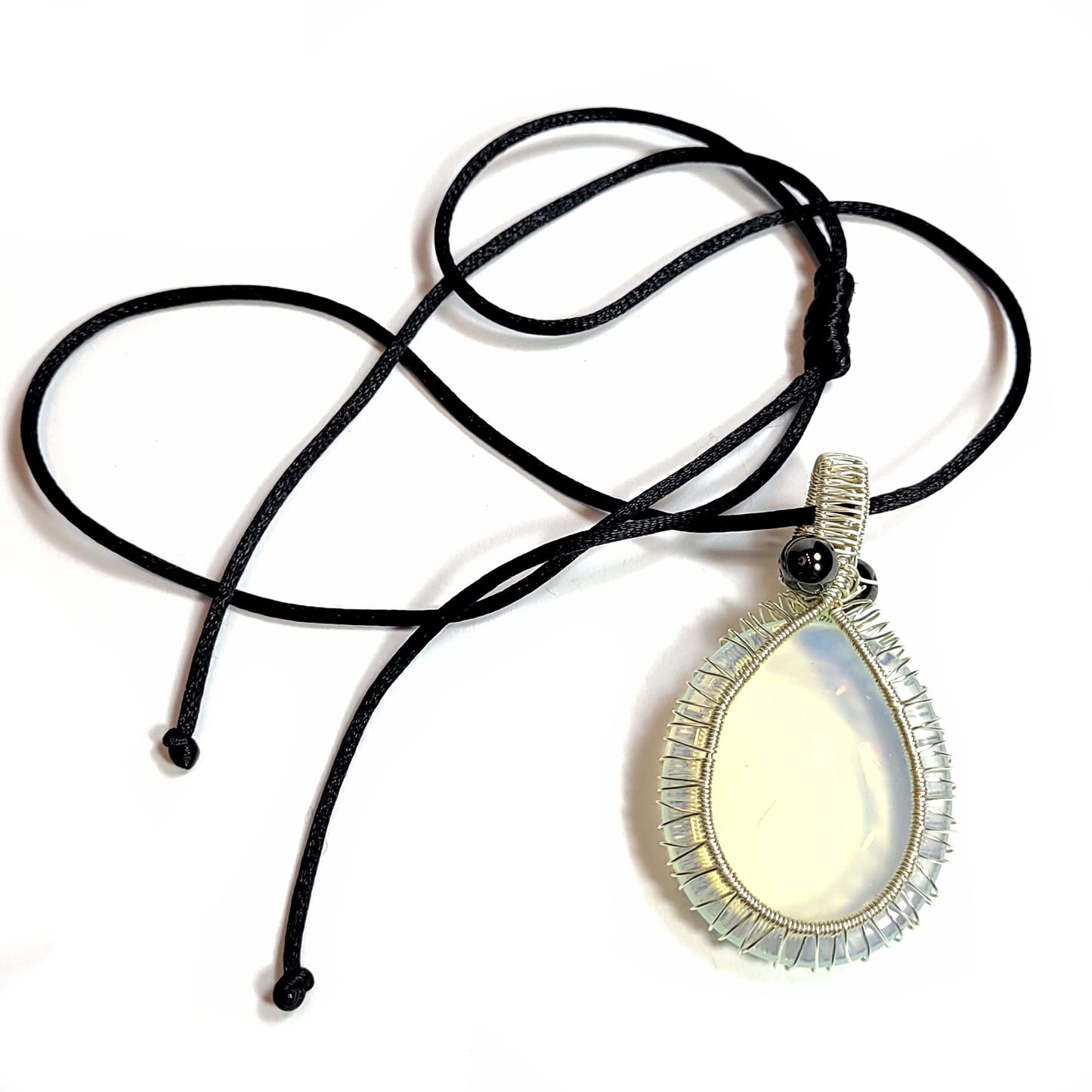 Silver toned wire wrapped Opalite. Comes with a black satin cord with an adjustable slip knot. This stone does have some specks and a scratch, but has very interesting color that really pops, especially on top of dark colors.