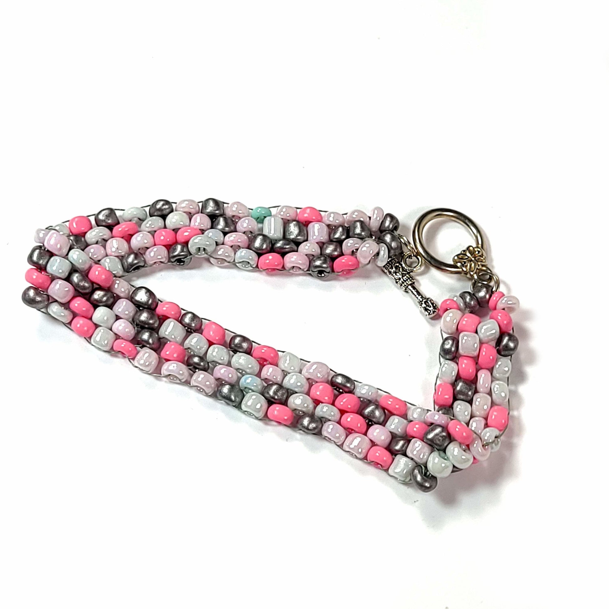 Bracelet made of irregular sized bright pink, white, pale pink, dark gray seed beads with one rebellious green bead. It has a toggle clasp.