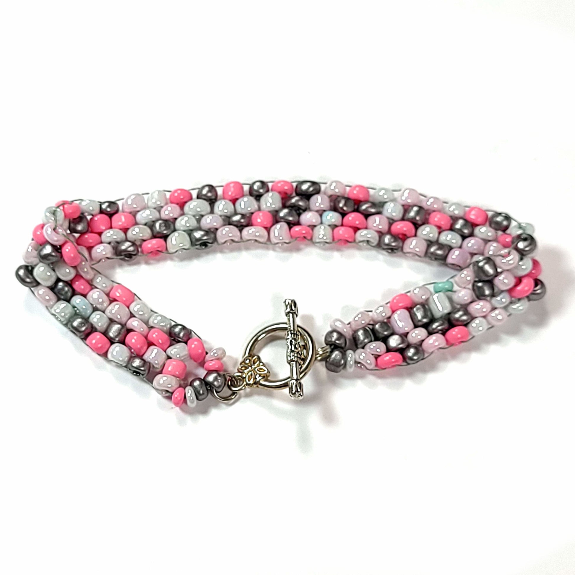 Bracelet made of irregular sized bright pink, white, pale pink, dark gray seed beads with one rebellious green bead. It has a toggle clasp.
