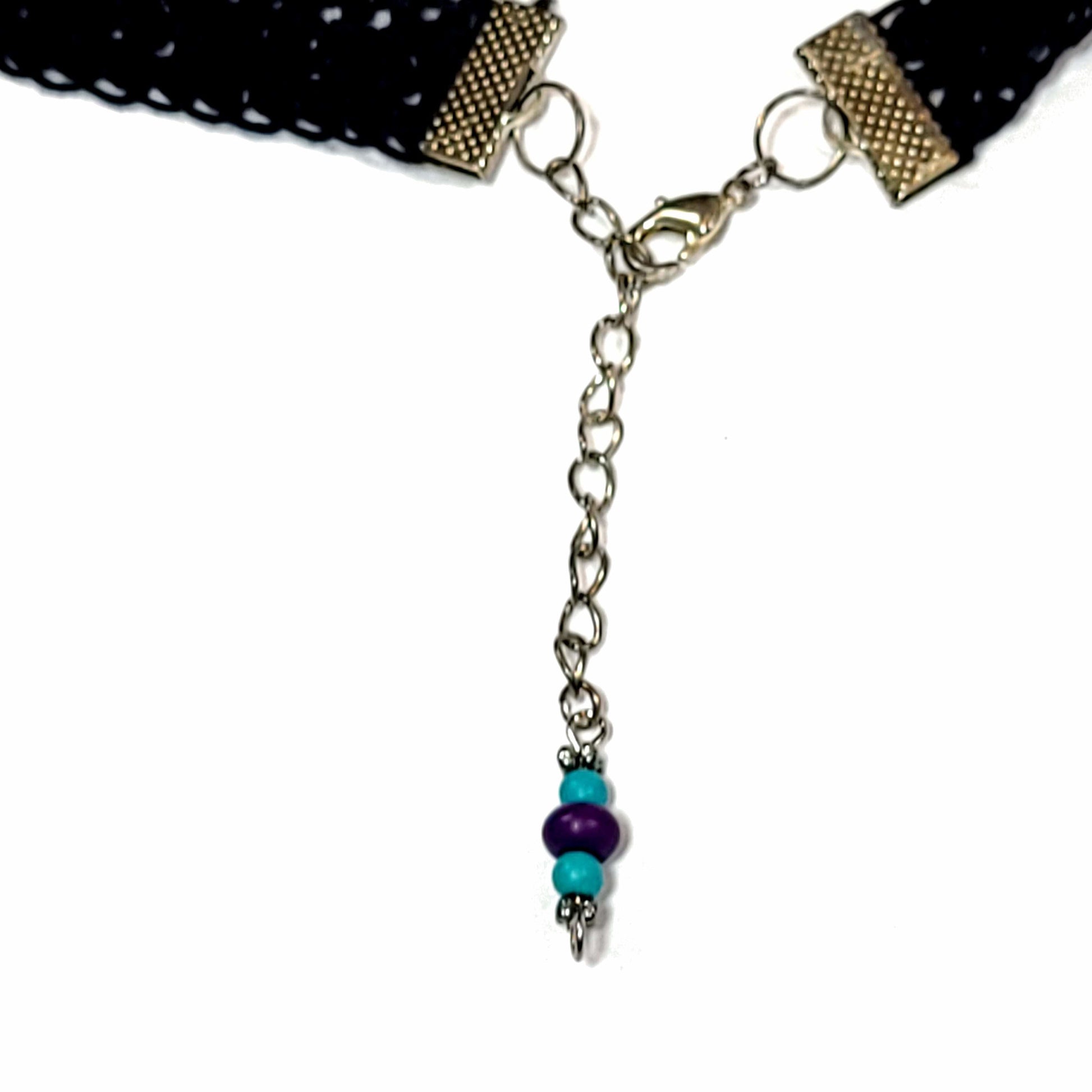 Clasp of the black choker with two blue beads and one larger purple bead.