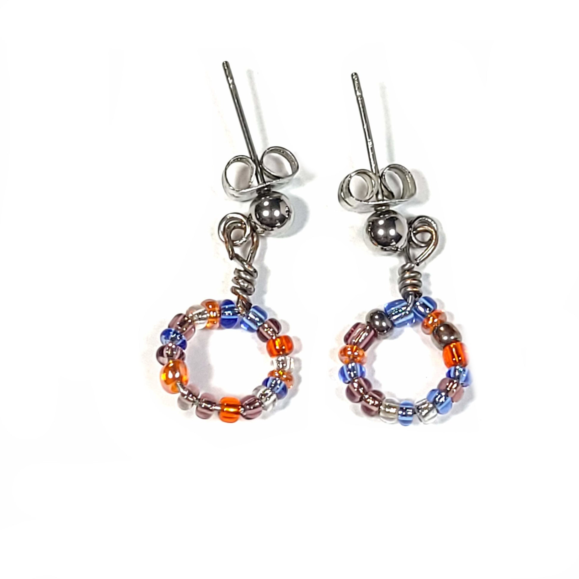 Bracelet and earring set made of multi-color seed beads in the blue and orange color range. The bracelets (2) are singular memory wire with triple lava rock center pieces. Small hoop earrings drop approximately.  Earrings only view.