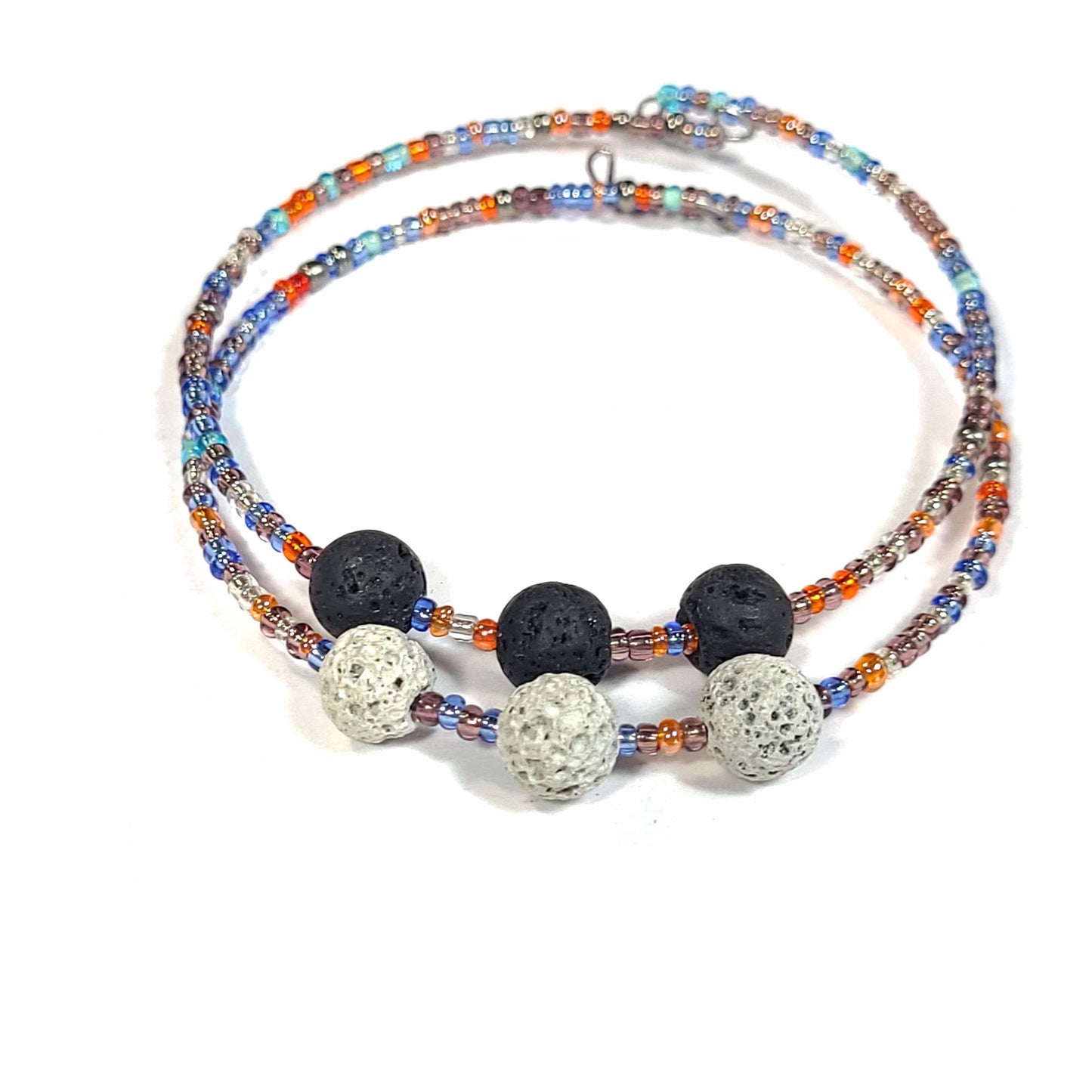 Bracelet and earring set made of multi-color seed beads in the blue and orange color range. The bracelets (2) are singular memory wire with triple lava rock center pieces. Small hoop earrings drop approximately. Bracelets only view.