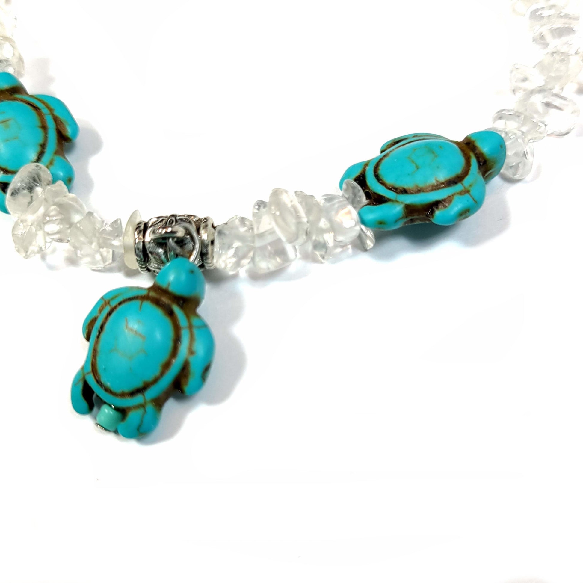 Close up view of a Necklace made of crystal quartz chips with aqua dyed howlite, with silver tone bale for center turtle and end caps. Silver tone extender chain and lobster clasp.