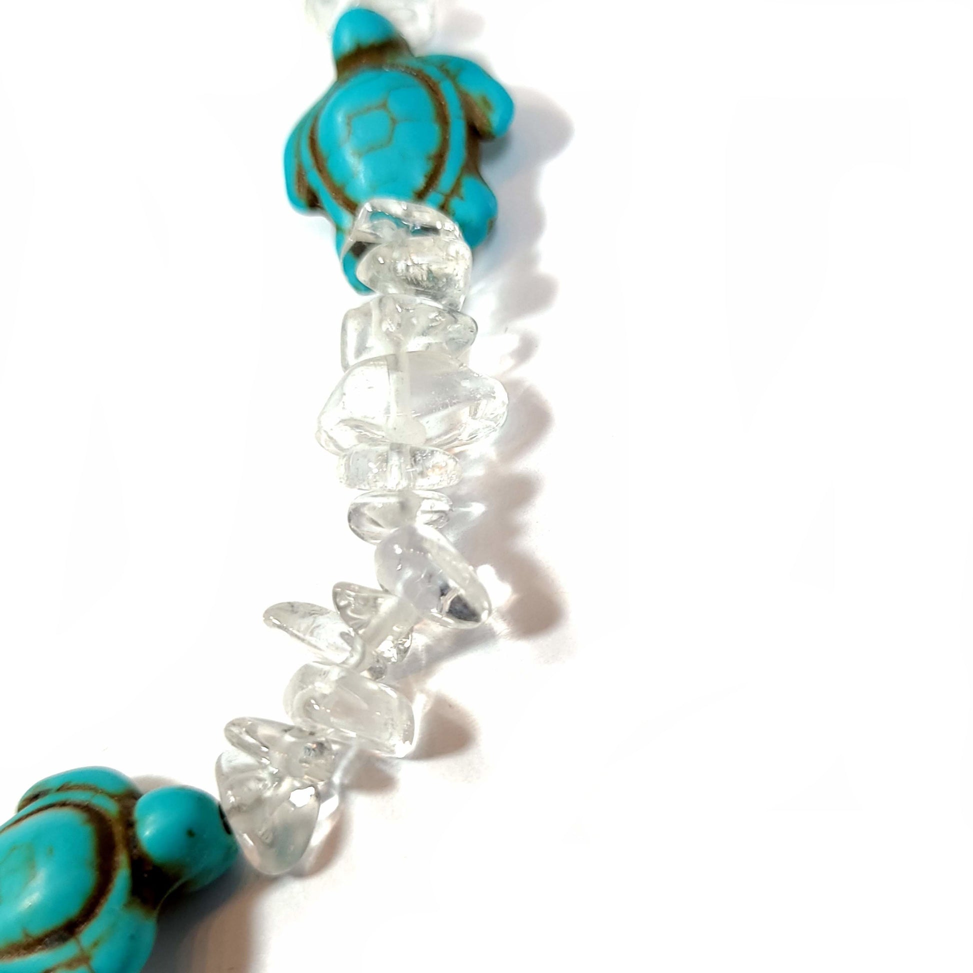 Close up of a Necklace made of crystal quartz chips with aqua dyed howlite, with silver tone bale for center turtle and end caps. Silver tone extender chain and lobster clasp.