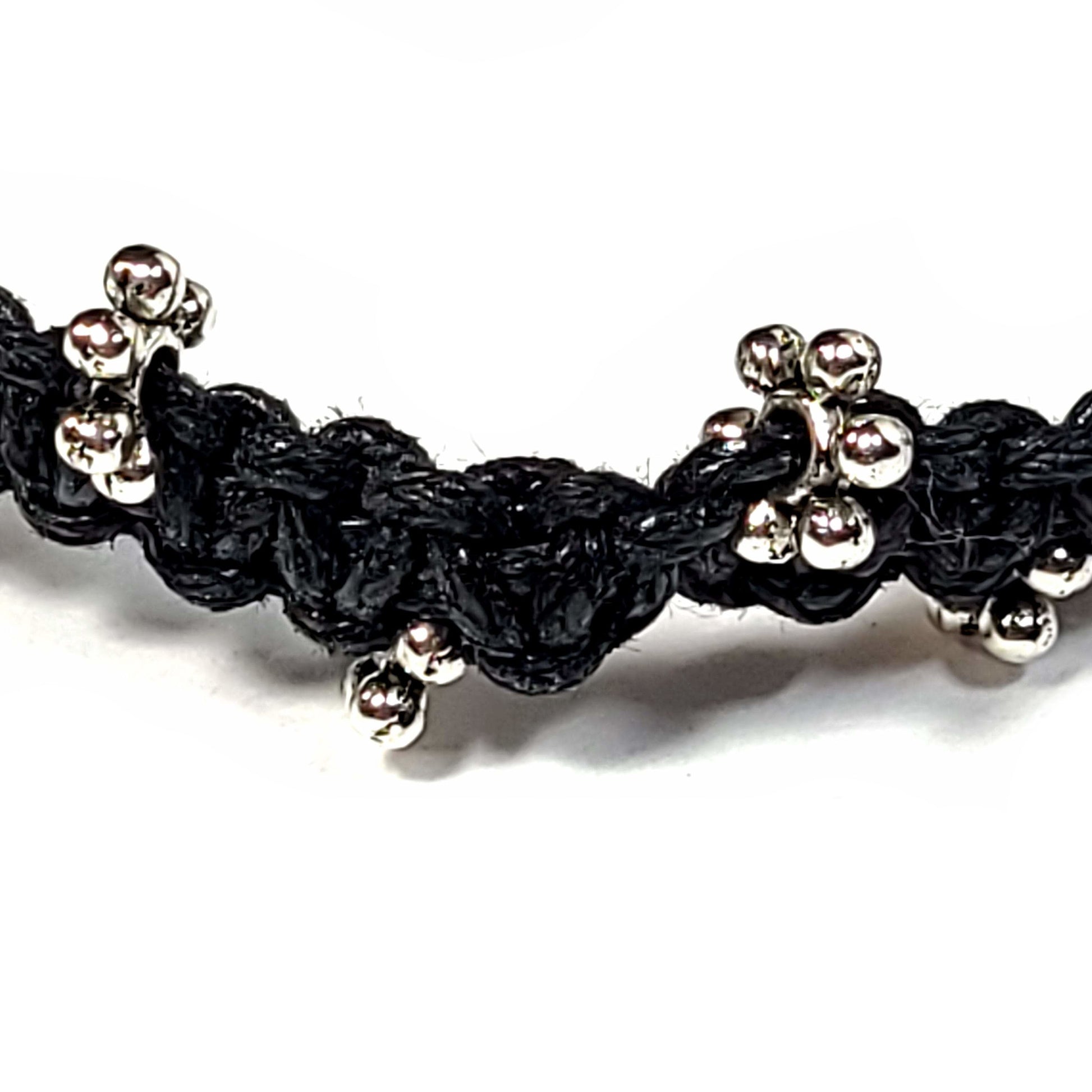 Close up of a Black macrame bracelet with silver spacer beads and a wooden bead clasp.